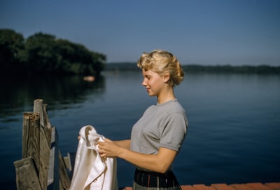 一个拿着白色纺织品的女人站在水面旁